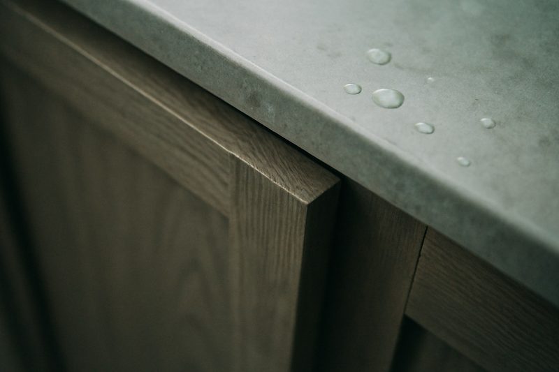 نمای نزدیک از لبهٔ درب کابینت روشویی چوبی با پوشش ضدرطوبت یکدست کنار چند قطرهٔ آب