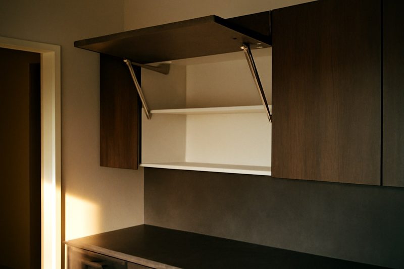کابینت بالای آشپزخانه با درب بالارونده باز و نگه‌داشته‌شده توسط جک گازی