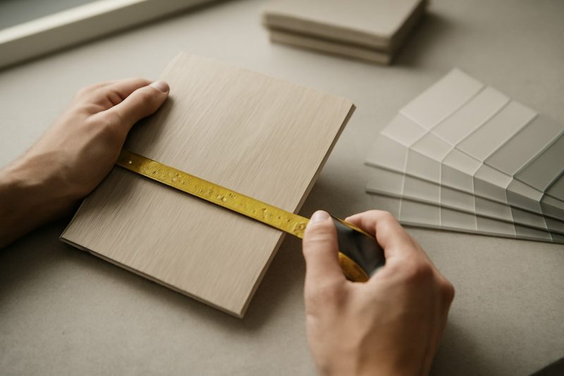 دست‌هایی در حال اندازه‌گیری با متر روی نمونهٔ رنگ چوب و طرح درب روی میز کارگاه