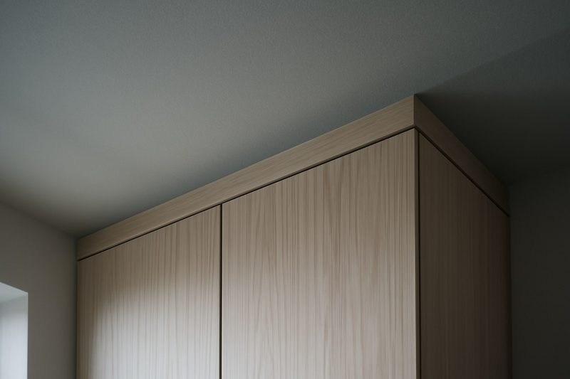 نمای نزدیک از لبهٔ بالایی کابینت چوبی آشپزخانه که دقیقا به سقف می‌رسد، بافت چوب و درز تمیز بین کابینت و سقف