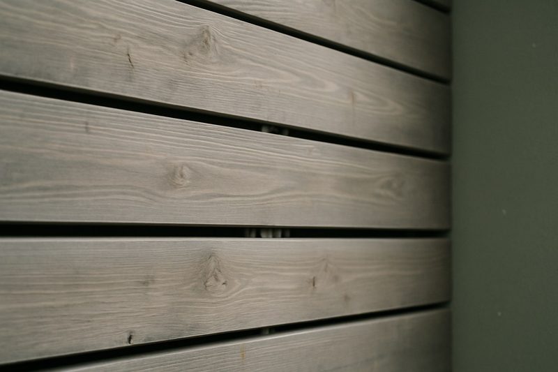 Close-up of thermowood boards fixed with hidden metal clips on a balcony wall with a narrow ventilation gap