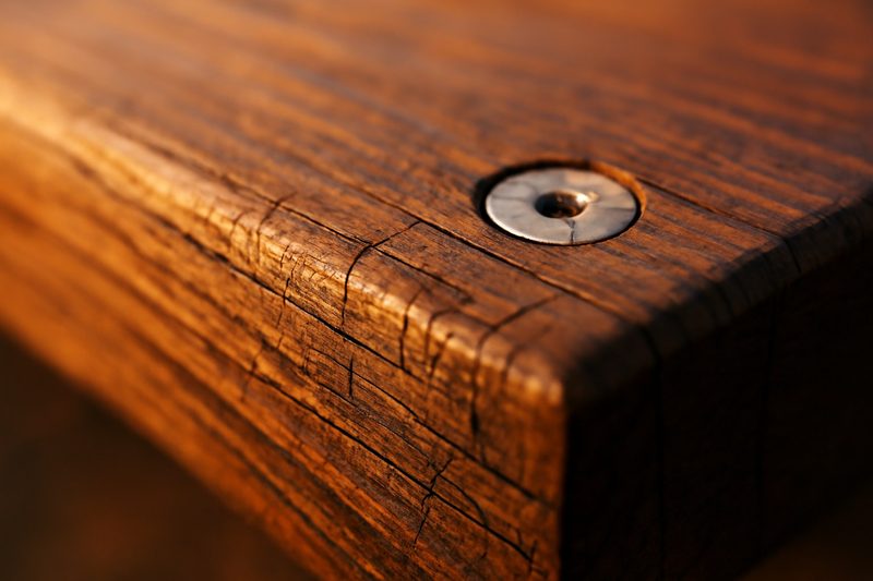 Close-up of a thermowood deck board end with fine surface checks and a stainless steel screw in a pre-drilled hole