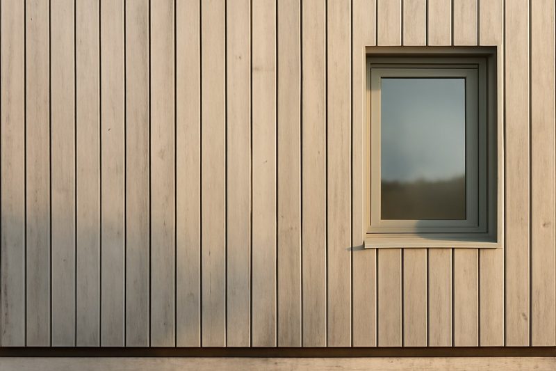 نمای نزدیک نمای چوبی مدرن یک ساختمان با باتن‌های عمودی و فاصلهٔ سایه در پایین کار نشان‌دهندهٔ تهویهٔ پشت نما