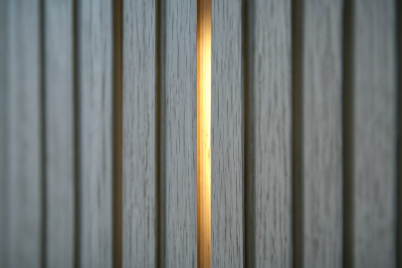 Close-up of vertical wood slat texture behind a TV with hidden backlighting