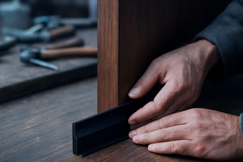 نصب یک نوار درزگیر سیلیکونی روی لبهٔ پایین یک درب چوبی در کارگاه